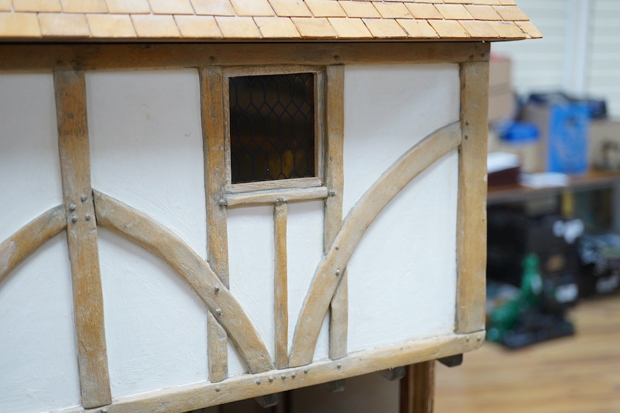 A modern doll’s house in the form of an oak framed Tudor house on three floors, with a shop on the ground floor, removable front panels on each floor and one side of the roof, with internal detailing and a good selection